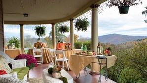 A covered patio with wicker furniture, a table set for dining, and potted plants. - Margaretville Mtn Inn B&B and Village Suites (Margaretville)