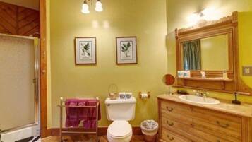 A bathroom with a wooden vanity, a white toilet, and two framed botanical prints on the wall.