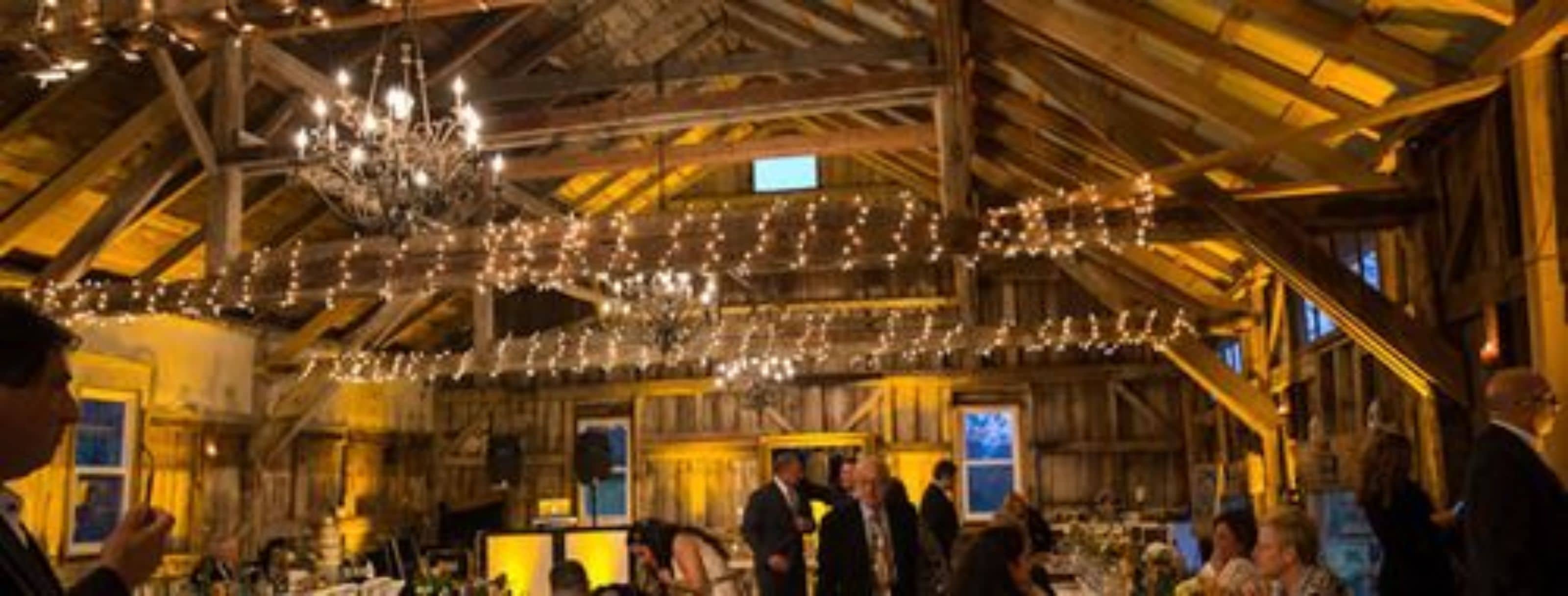 A rustic interior with exposed wooden beams, a chandelier, and string lights.