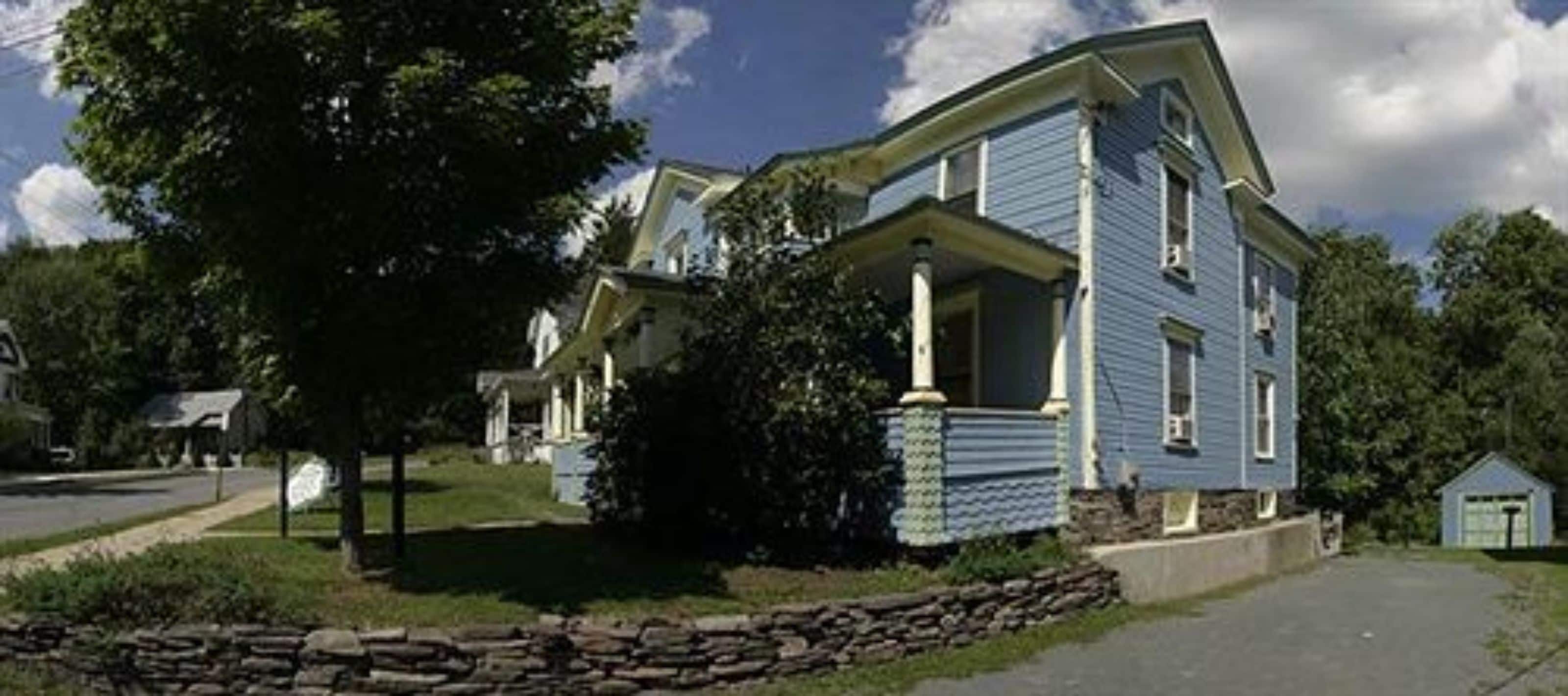 A two-story blue house with a stone foundation, a front porch, and a small garage.