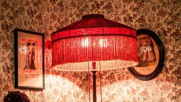 A room with floral wallpaper, a framed picture, and a red lamp.