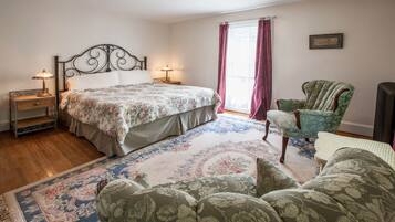 A bedroom with a bed, two bedside tables with lamps, a green armchair, a patterned rug, and a window with curtains.