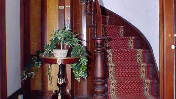 A wooden staircase with a red carpet, a wooden door, and a table with a plant.