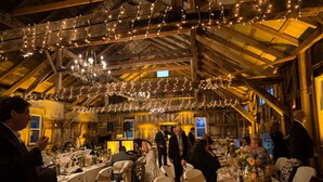 An indoor venue with wooden beams and a high ceiling, decorated with string lights and a chandelier. Tables are set for a formal event, with guests seated and some standing. - Margaretville Mtn Inn B&B and Village Suites (Margaretville)