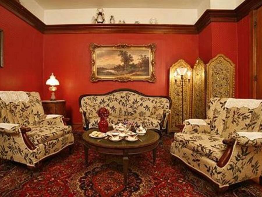 A room with a red wall, two floral armchairs, a round table with tea sets, and a framed landscape painting.