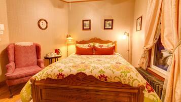 A bedroom with a wooden bed, a pink armchair, a bedside table with a lamp, and framed pictures on the wall.