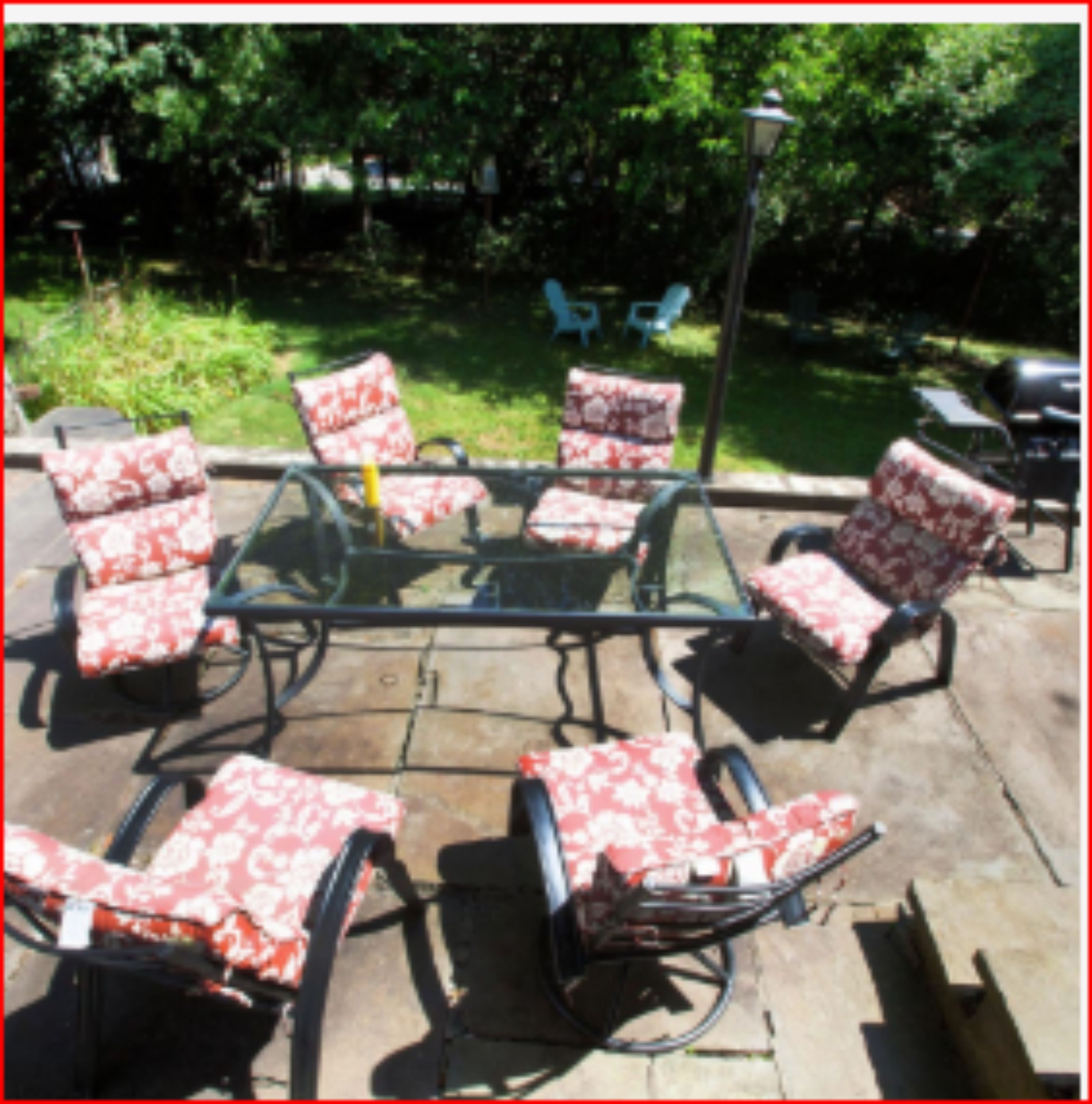 Een terras met vier stoelen en een tafel, omgeven door groen.