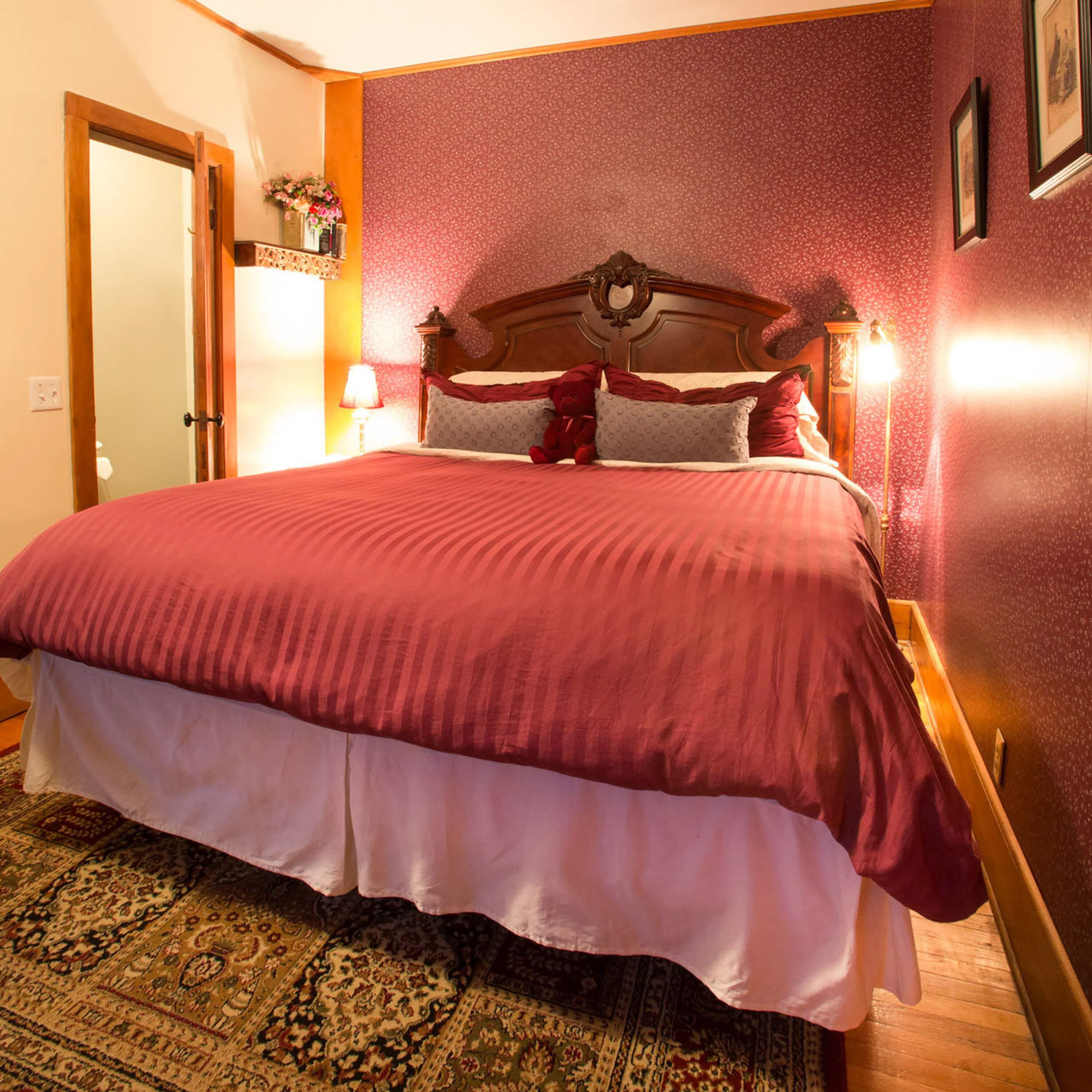 A neatly made bed with a red and white bedspread, a wooden headboard, and a decorative wall hanging above it.