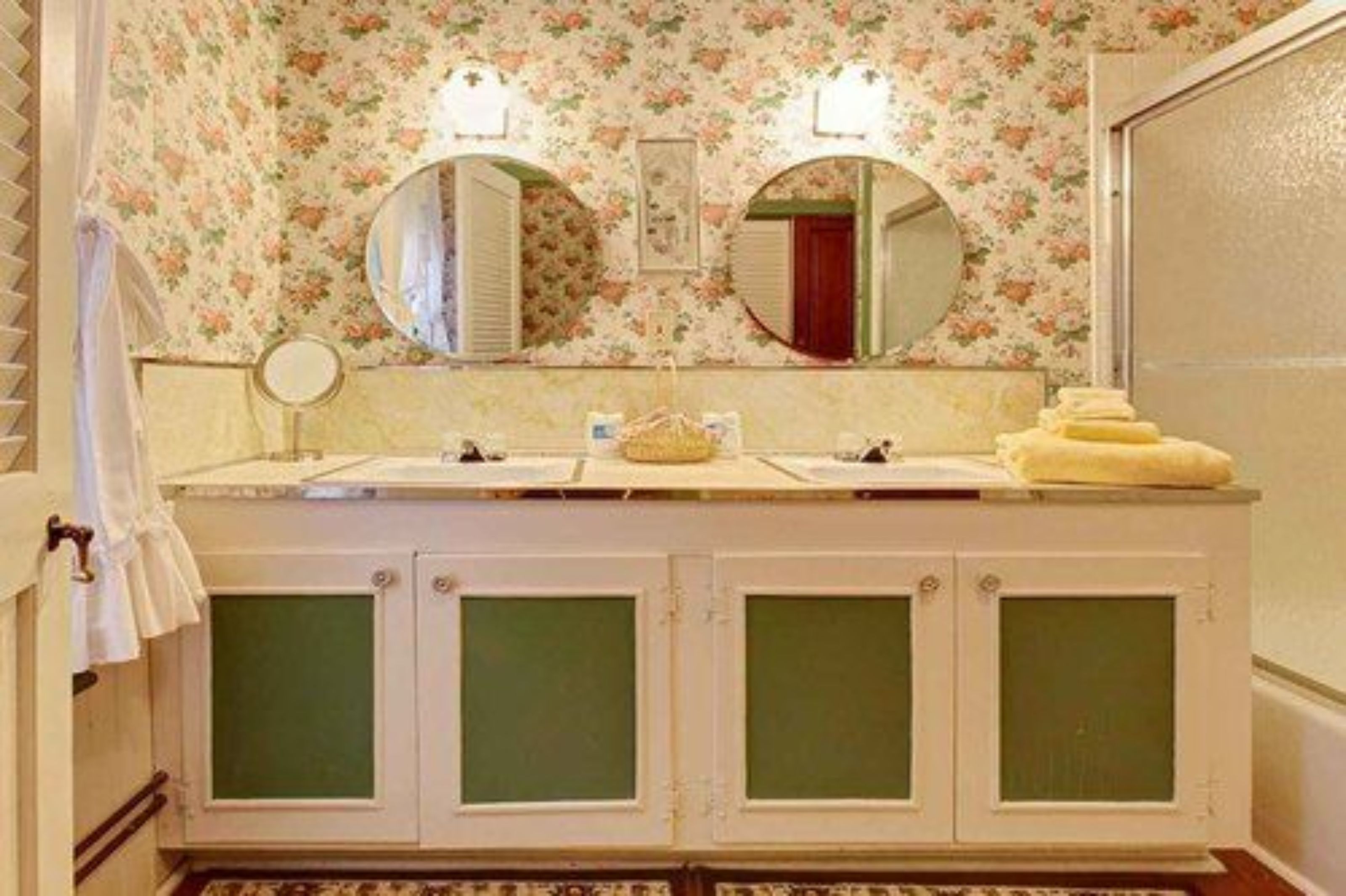 Un baño con papel tapiz floral, un tocador doble y un espejo sobre el lavabo.