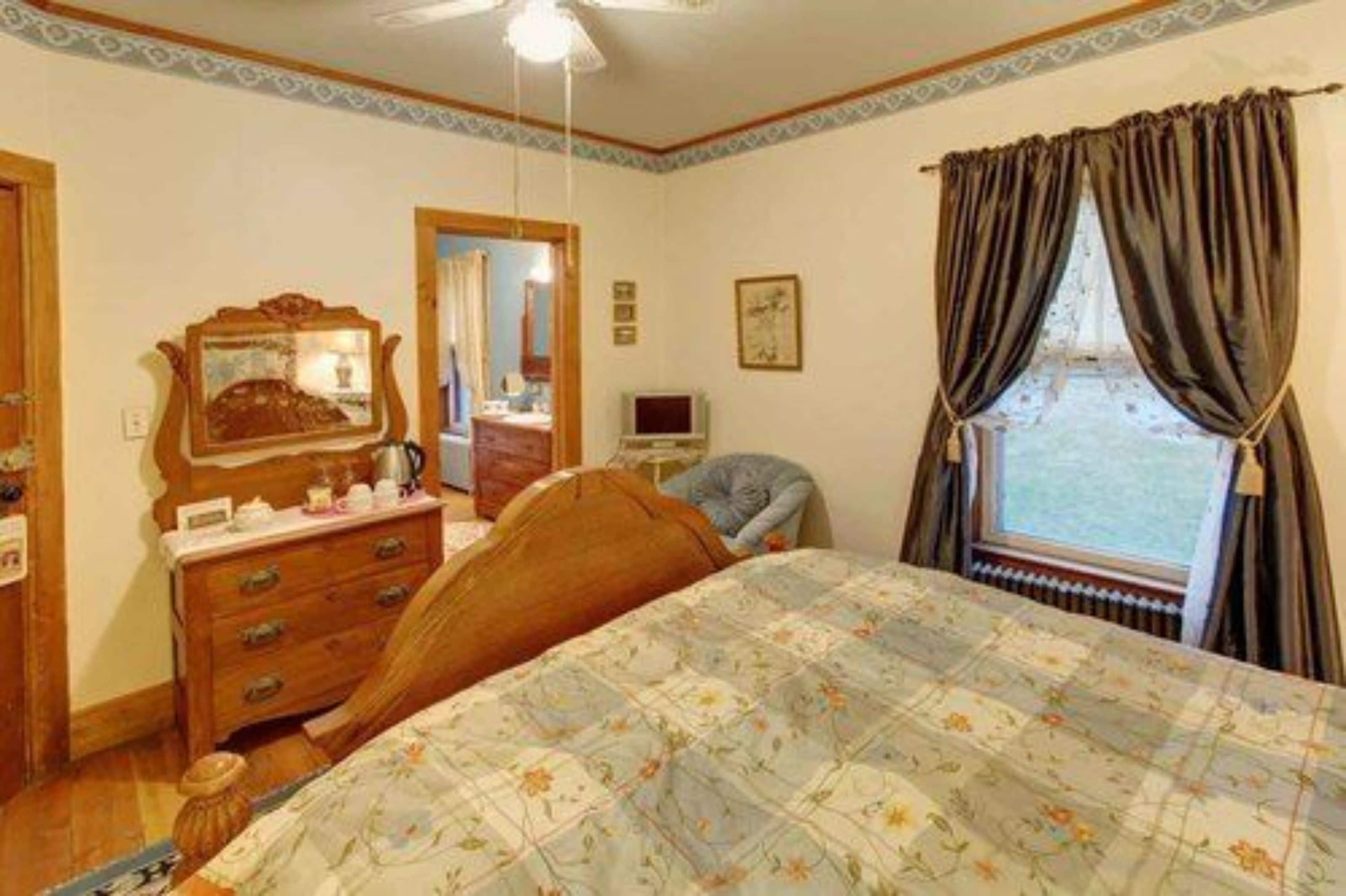 Een slaapkamer met een houten bed, een dressoir, een spiegel, een televisie en een raam met gordijnen.