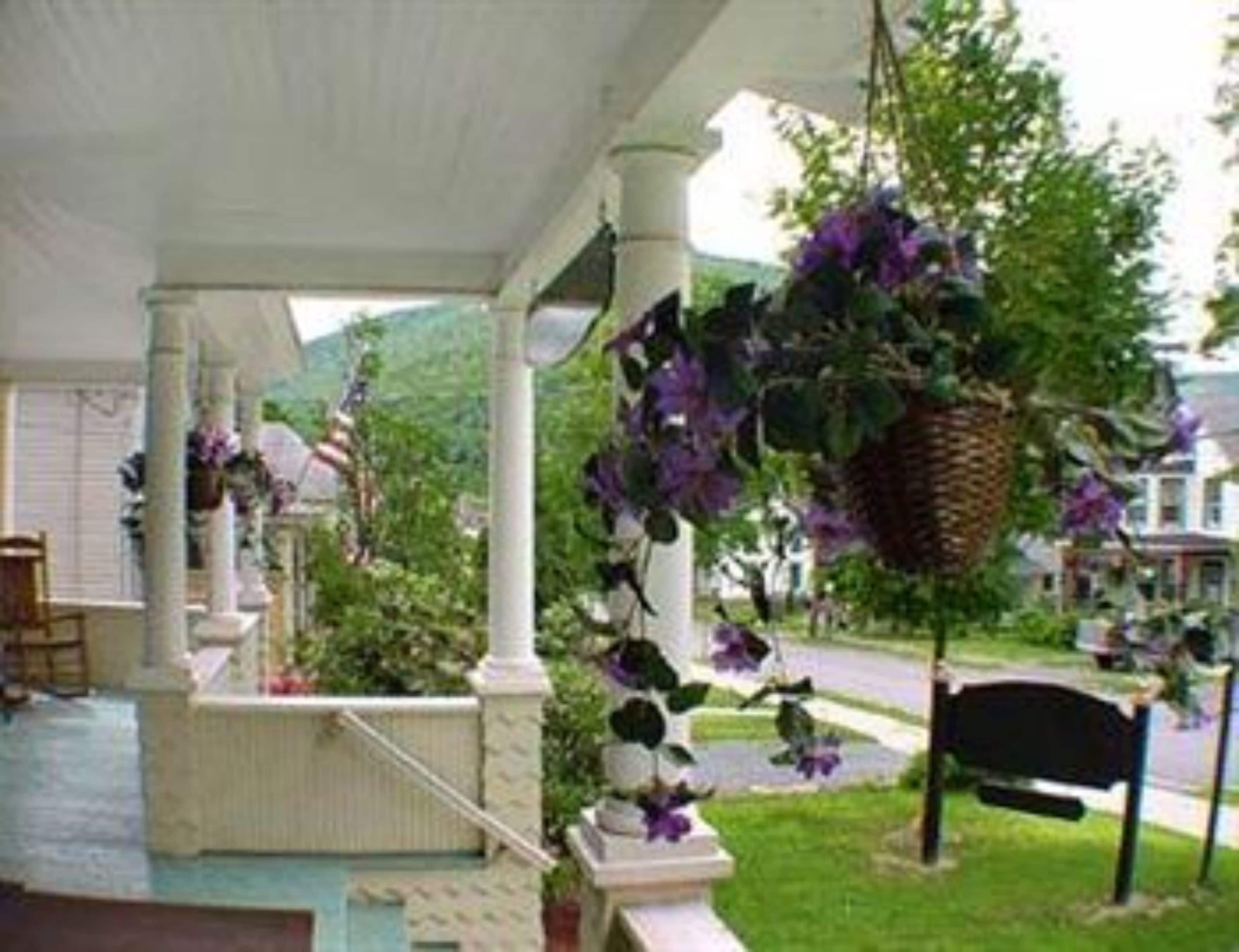 Un porche cubierto con un banco, cestas de flores colgantes y vista a una calle residencial.