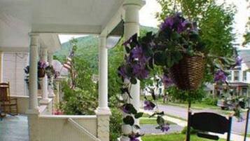 Un porche cubierto con un banco, cestas de flores colgantes y vista a una calle residencial.