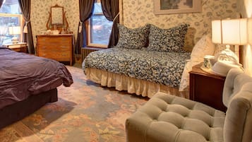 Un dormitorio con cama, cómoda y silla, con papel tapiz floral y vistas a través de la ventana.