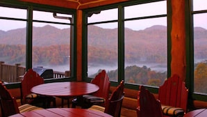 A wooden interior with a round table and chairs, large windows offering a view of a forested mountain range. - Wildberry Lodge (Leicester)