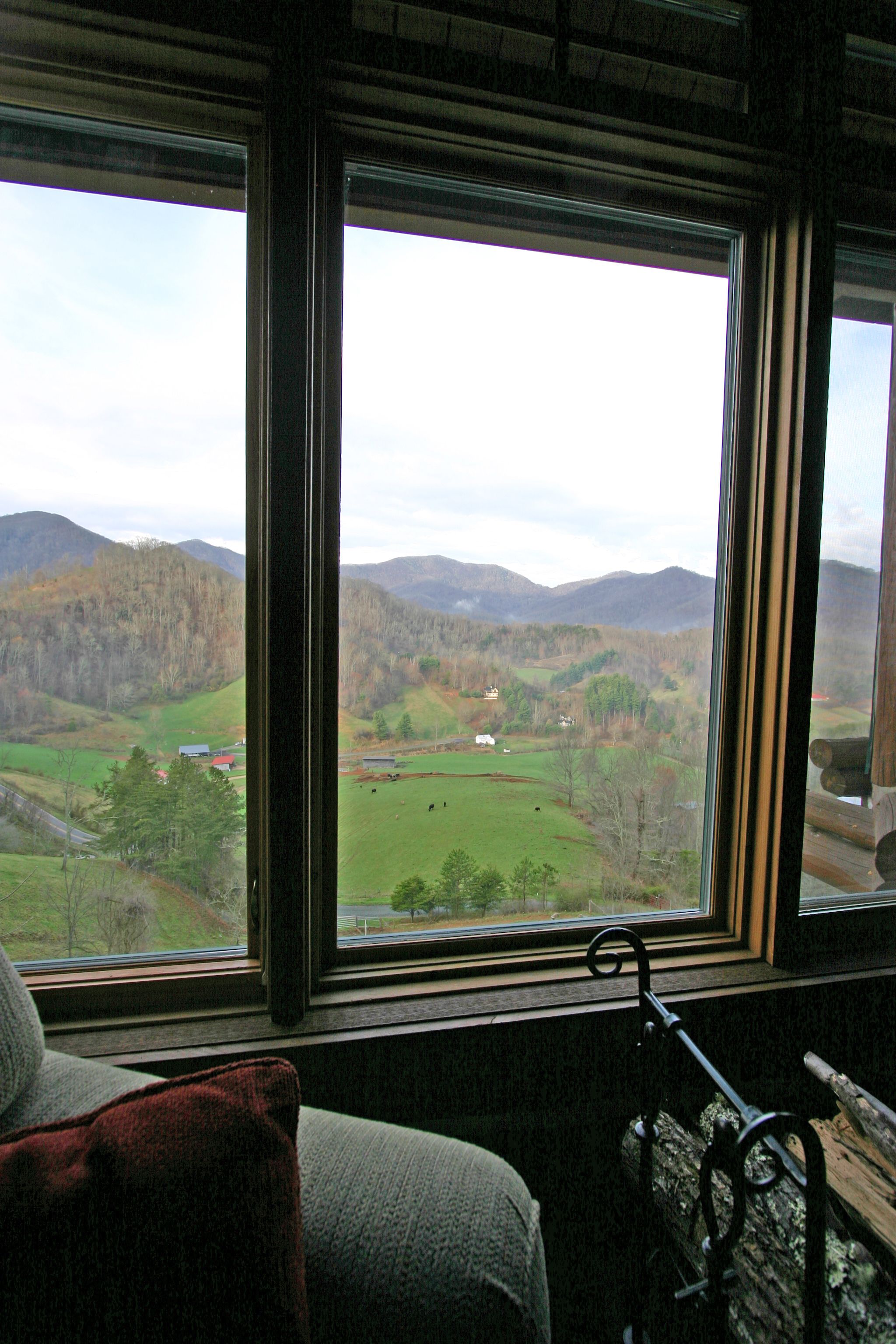 A room with a large window overlooking a valley with mountains and a green field.