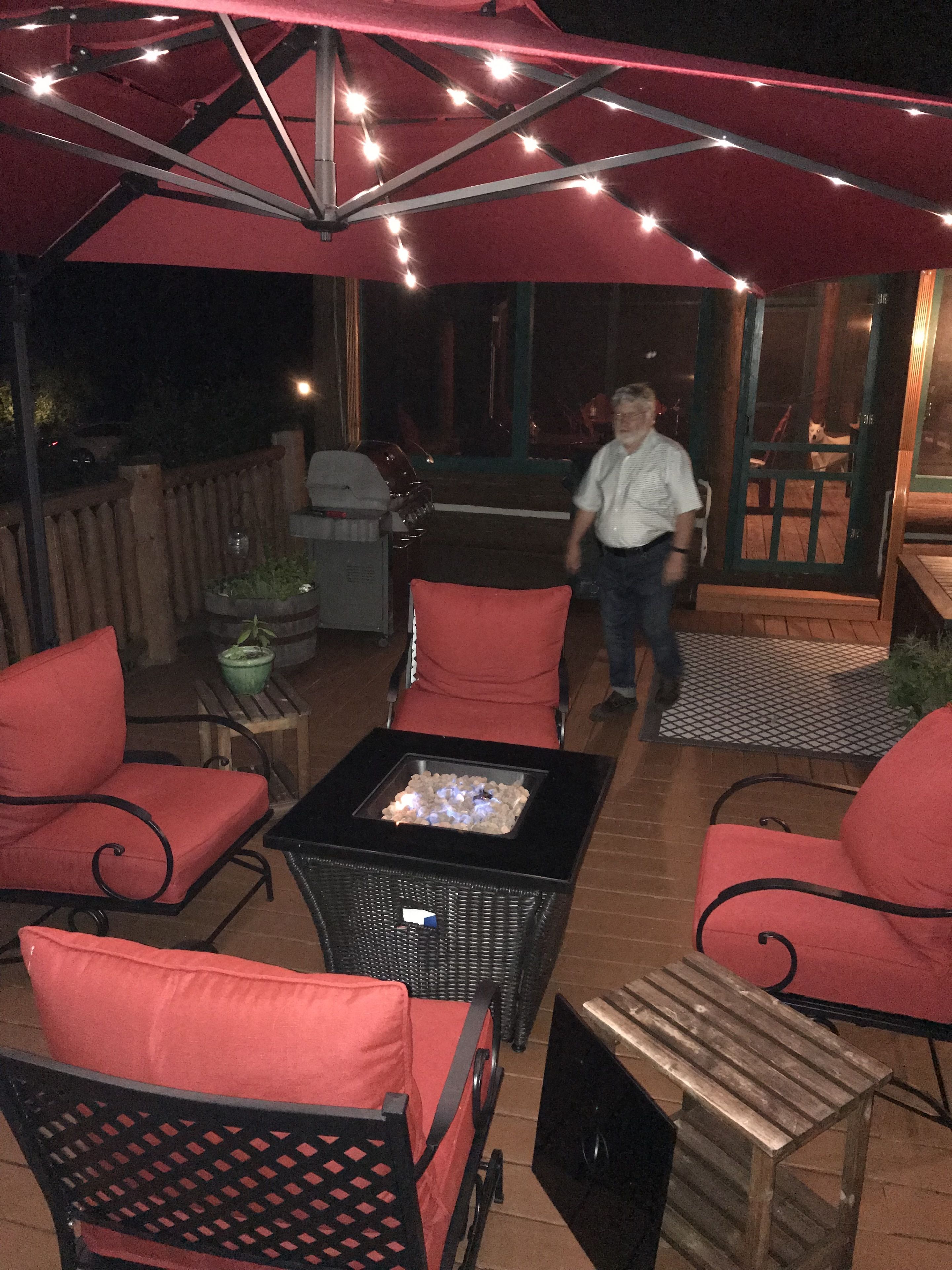 Un patio al aire libre con una mesa de fogata, sillas rojas acolchadas y una mesa de madera.