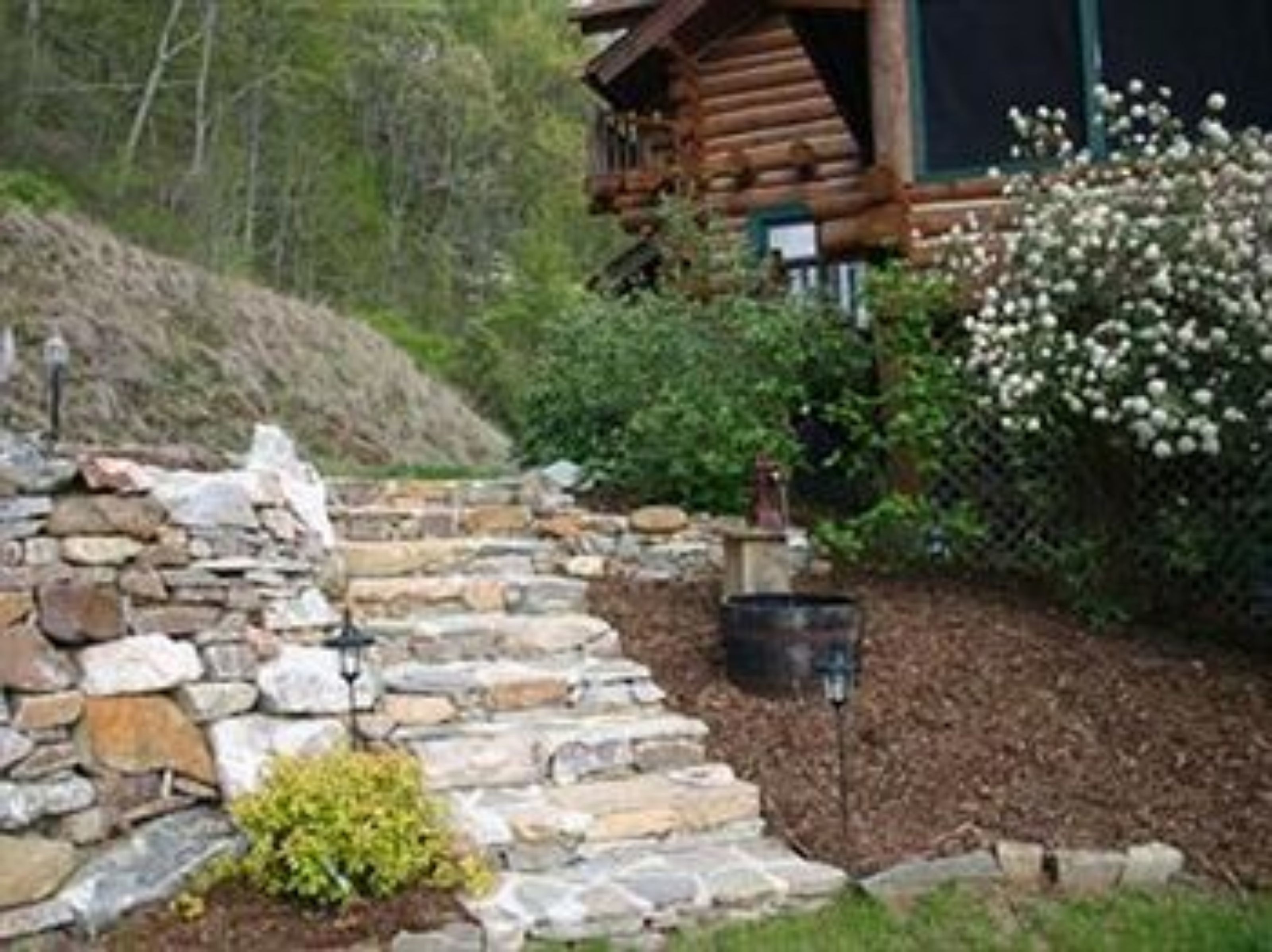 A log cabin with a stone staircase leading up to a wooden deck.