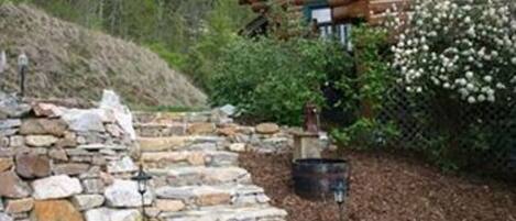 A log cabin with a stone staircase leading up to a wooden deck.