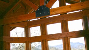A cozy cabin interior with a wooden ceiling, large windows offering mountain views, a leather sofa, and a dining area with chairs. - Wildberry Lodge (Leicester)