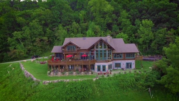 A large, two-story log cabin with a deck and outdoor seating area, surrounded by dense forest. - Wildberry Lodge (Leicester)