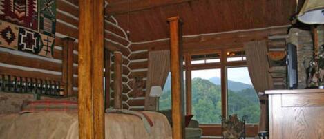 Una habitación tipo cabaña de madera con una cama, una ventana con vistas a la montaña y un escritorio de madera.