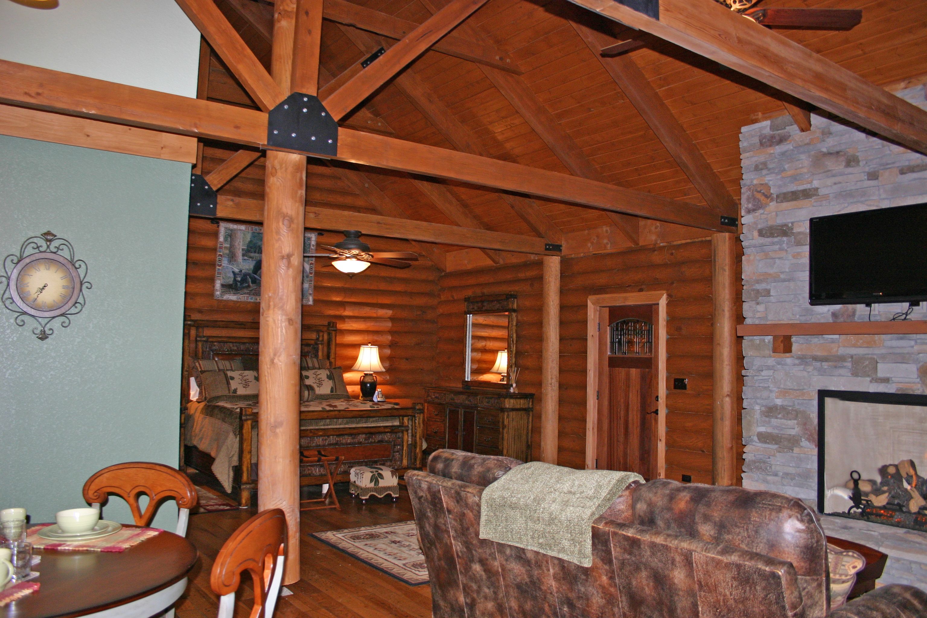 L’intérieur chaleureux d’un chalet avec des poutres en bois, une cheminée en pierre, un coin repas et un téléviseur fixé au mur.