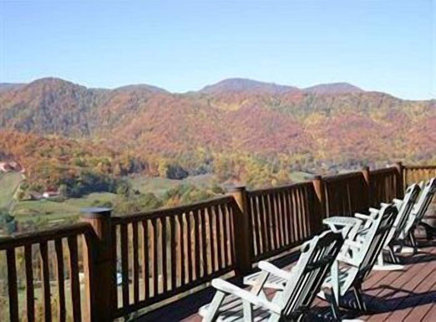 Eine Terrasse mit Holzgeländern und weißen Stühlen mit Blick auf eine gebirgige Landschaft.