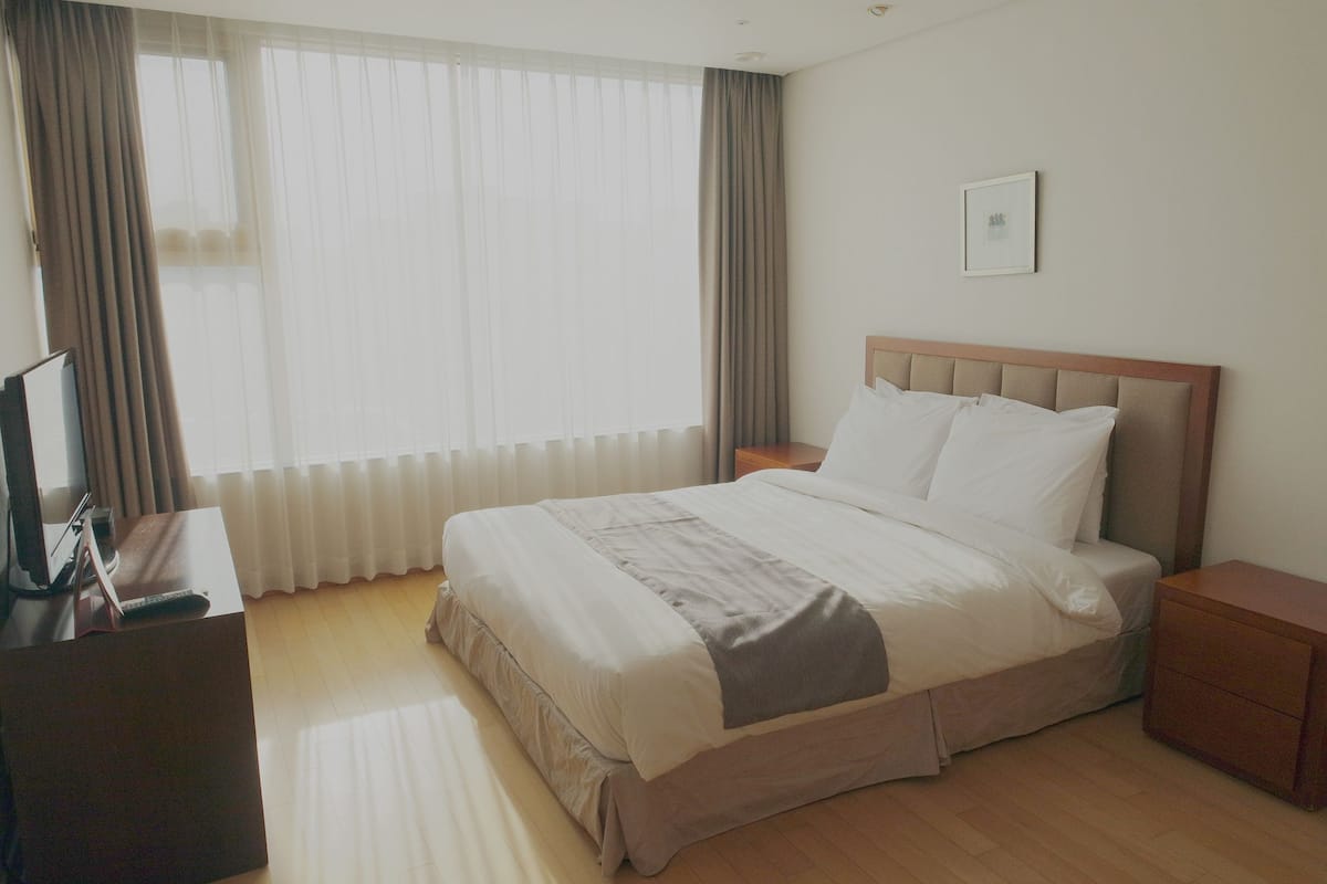 Une chambre d’hôtel avec un lit, une table de chevet, une télévision et une fenêtre avec des rideaux.