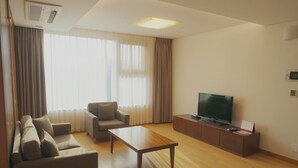 Een moderne woonkamer met een bank, fauteuil, salontafel, televisie en houten vloer.