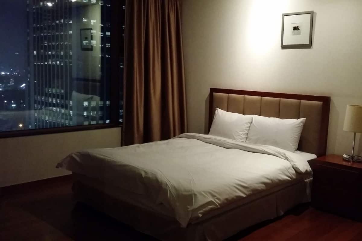 Une chambre d’hôtel avec un lit, une table de chevet, une lampe, une fenêtre avec des rideaux et un tableau encadré au mur.