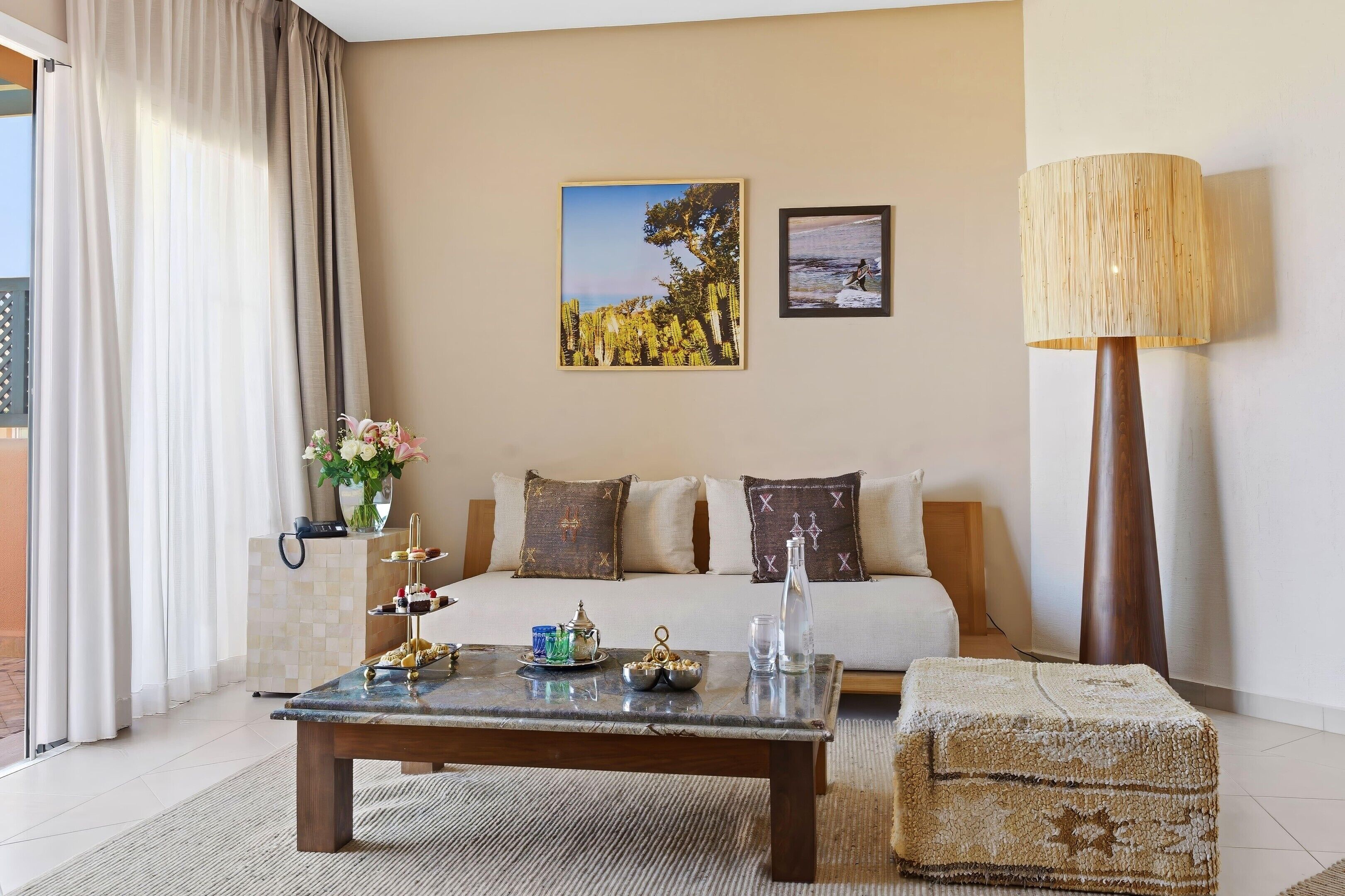 A hotel room with a bed, a coffee table with snacks, a lamp, and two framed pictures on the wall.