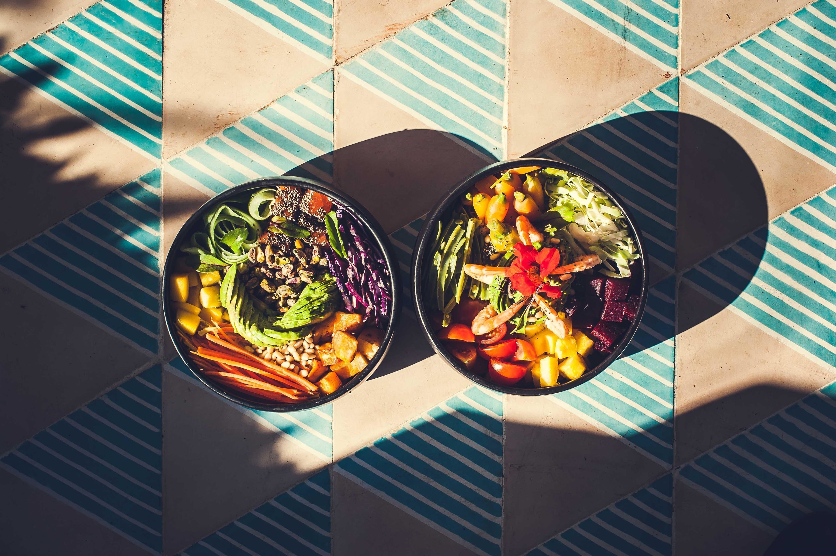 Two bowls of salad on a tiled floor with a geometric pattern.