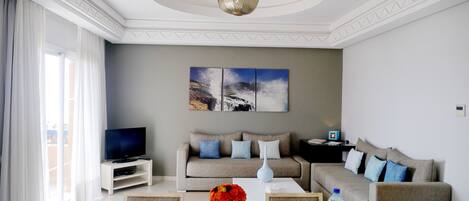 A modern living room with a sofa set, a flat-screen TV, a coffee table with a vase of flowers, and a painting on the wall.