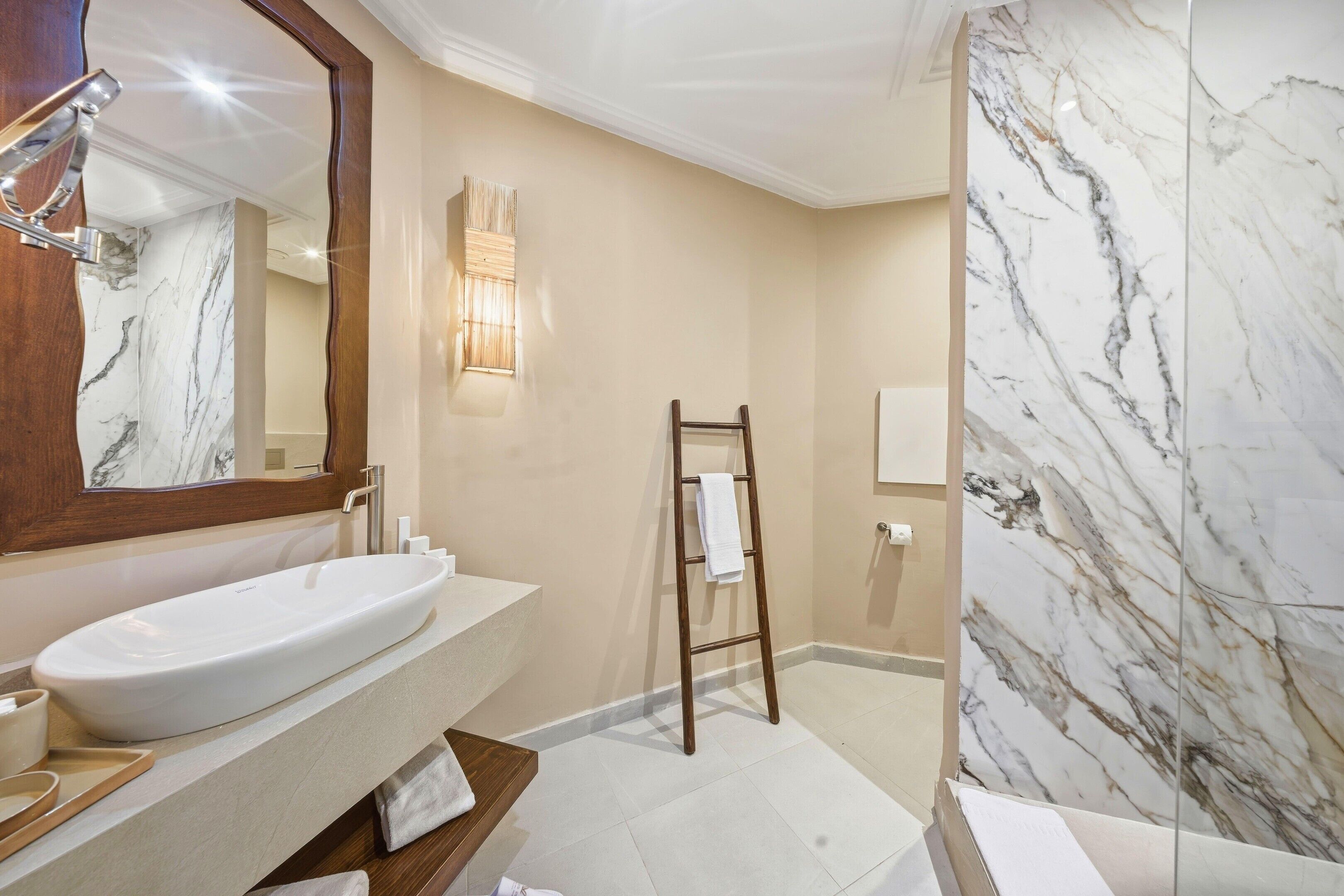 A bathroom with a large white sink, a wooden ladder, and a marble shower wall.