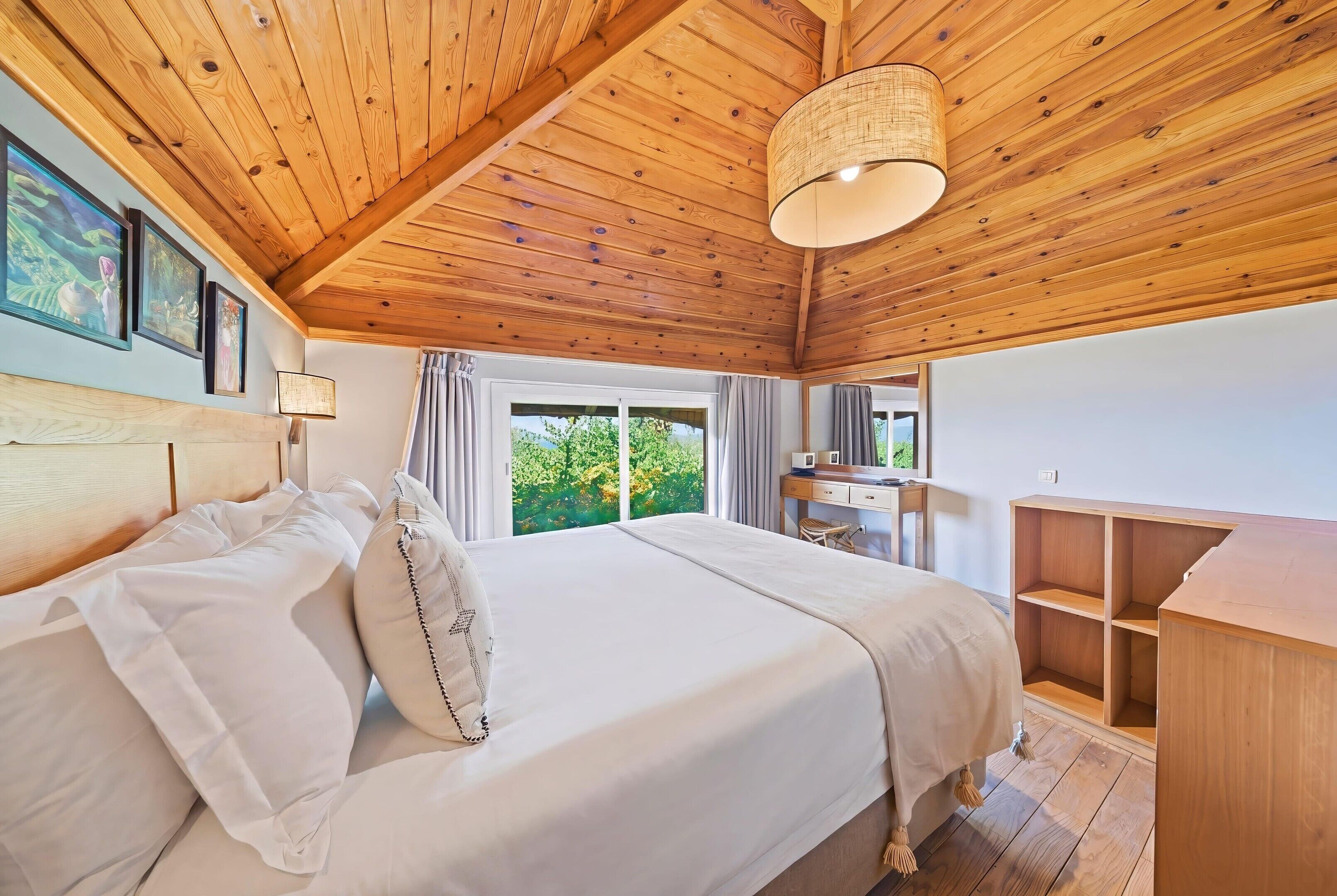 A bedroom with a wooden ceiling, a bed with white linens, a desk, and a window with curtains.