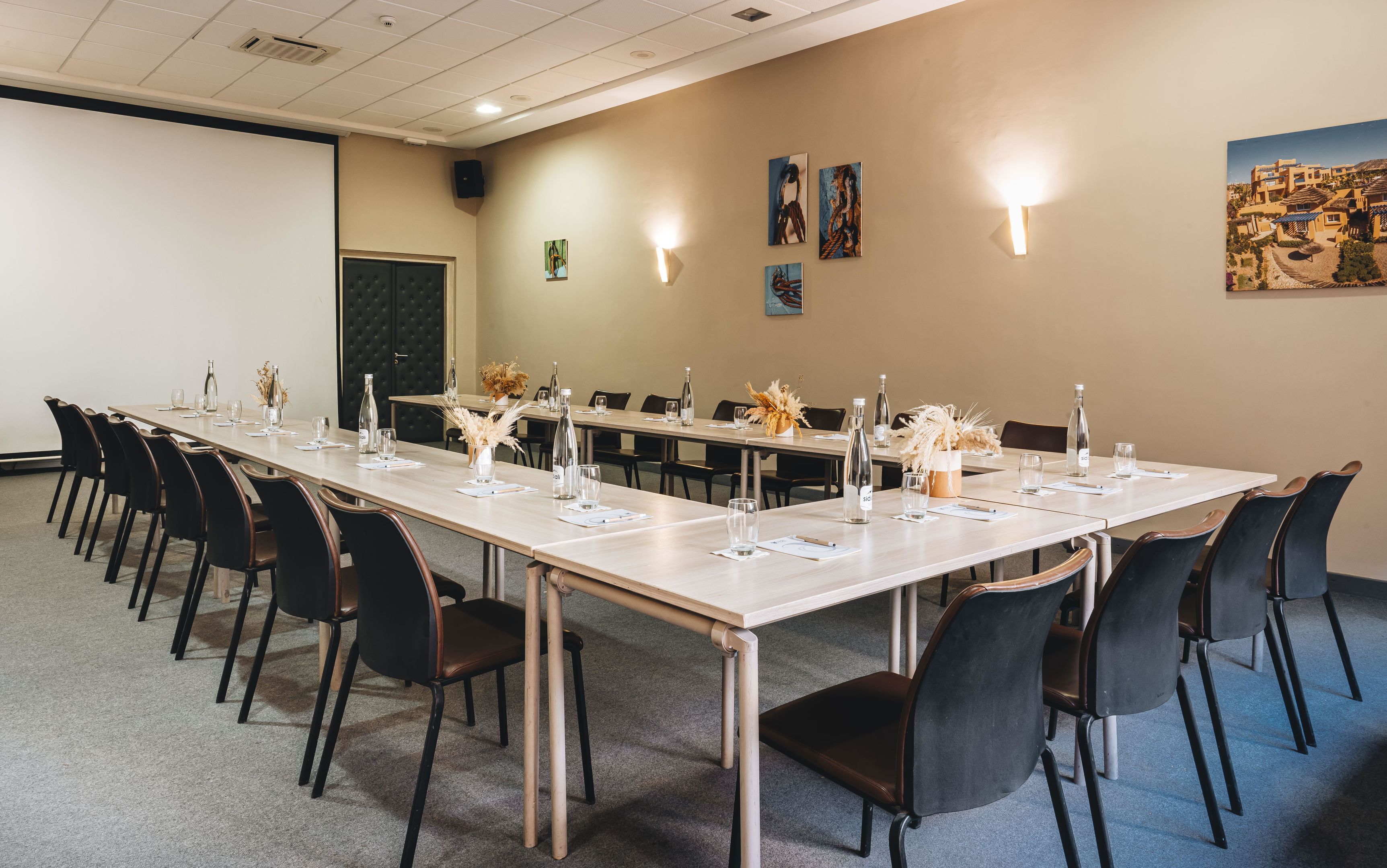 Un salón de conferencias con mesas largas, sillas y una pantalla para proyector.