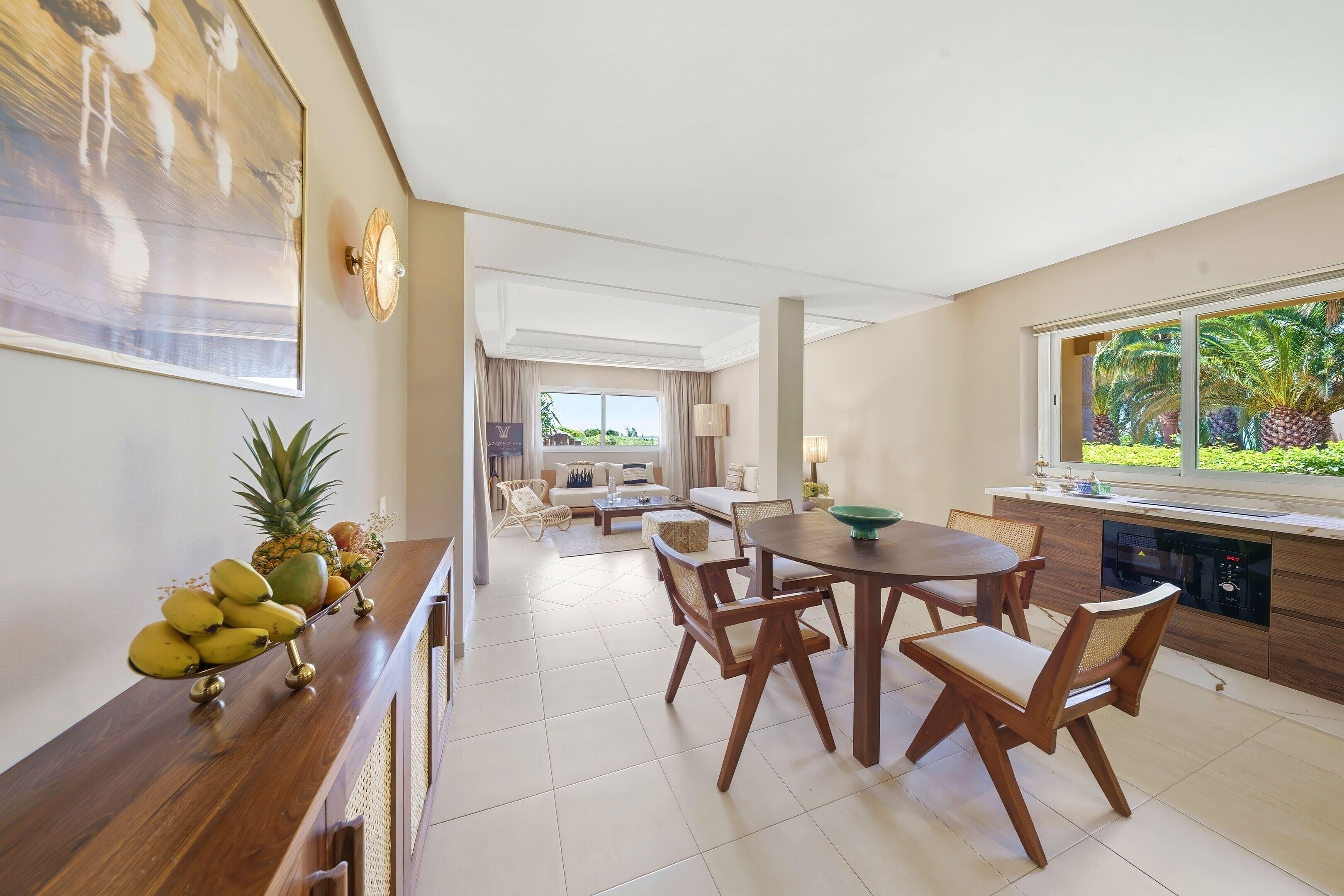 Un comedor con una mesa y sillas de madera, una cocina con lavavajillas integrado y vistas a zonas verdes a través de una ventana.