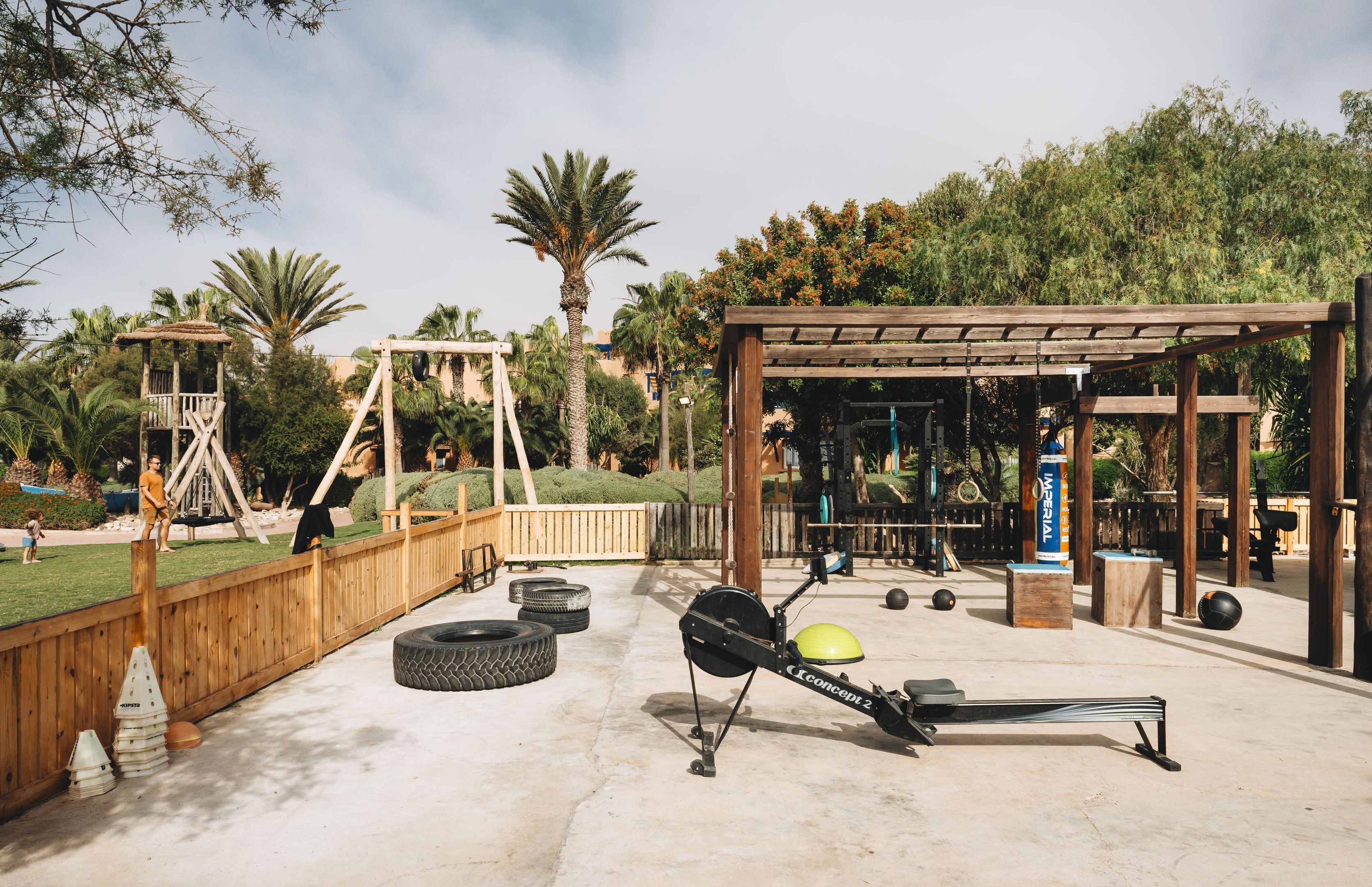 Un área de gimnasio al aire libre con equipo de ejercicio, una terraza de madera y un conjunto de columpios.