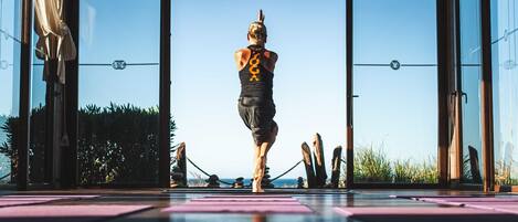 Una persona realizando una postura de yoga sobre una colchoneta en una habitación con ventanas grandes y vistas al exterior.