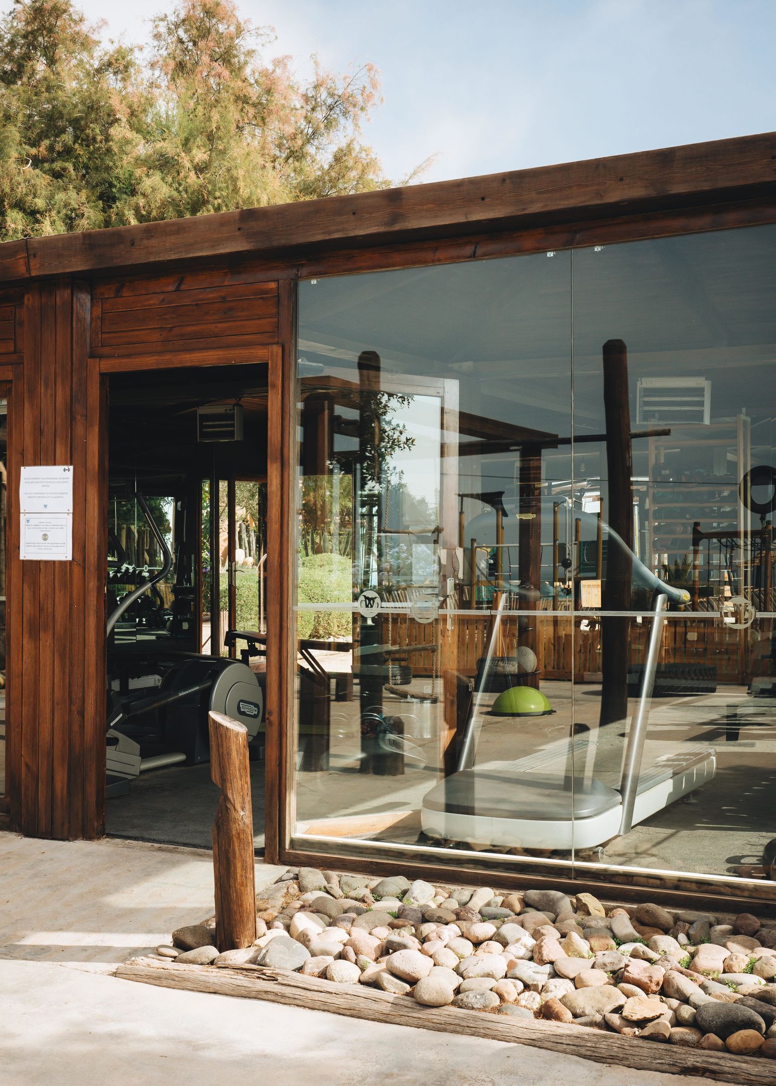 A modern building with a glass entrance, wooden exterior, and a gravel pathway leading to a bench.