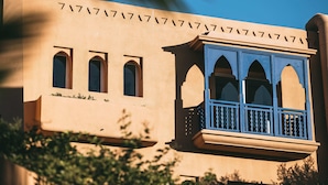 Un edificio de fachada color beige, tres ventanas arqueadas y un balcón con barandillas azules.