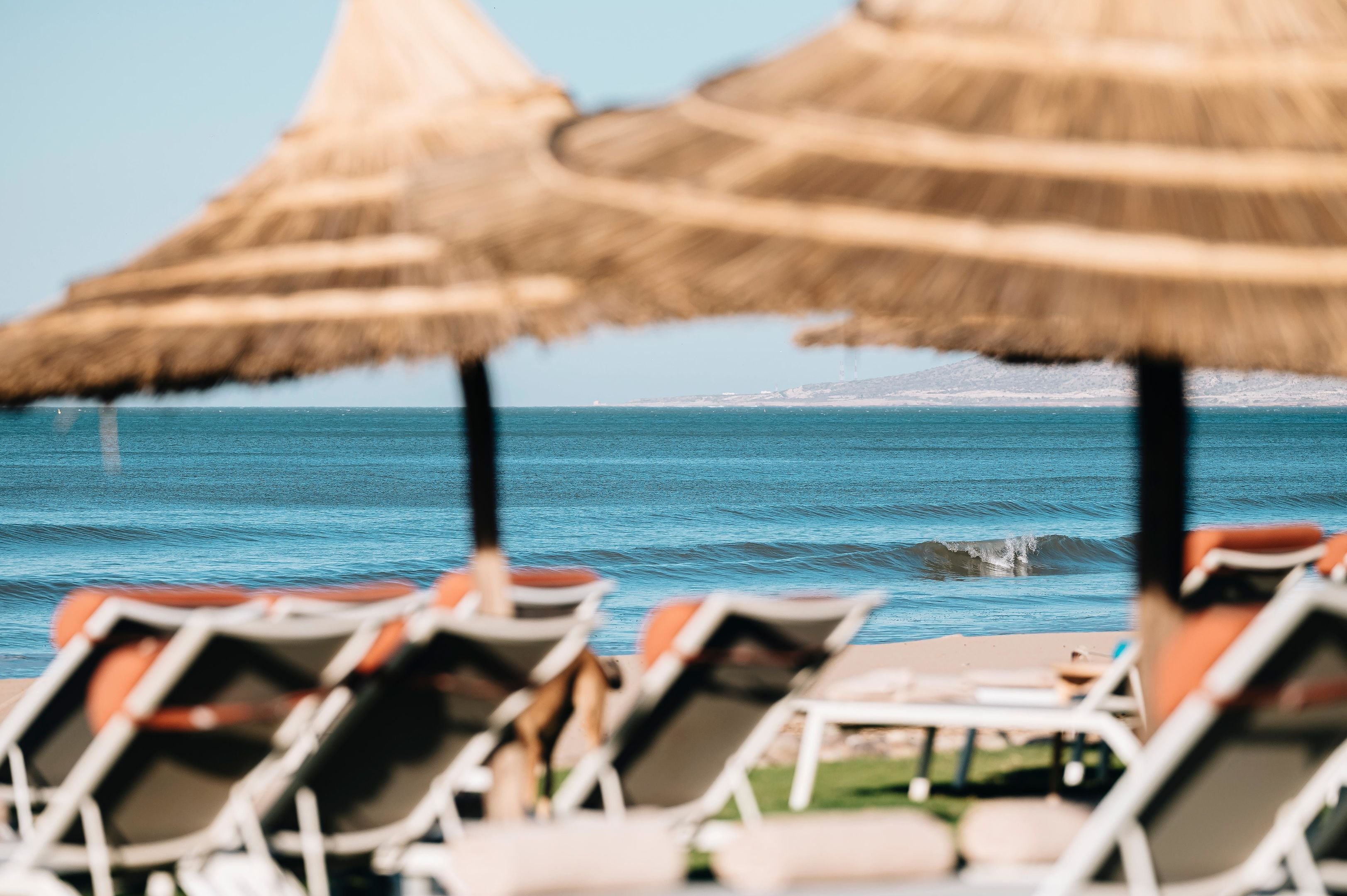 Una playa con sillas de descanso y sombrillas de paja, con vista al mar.