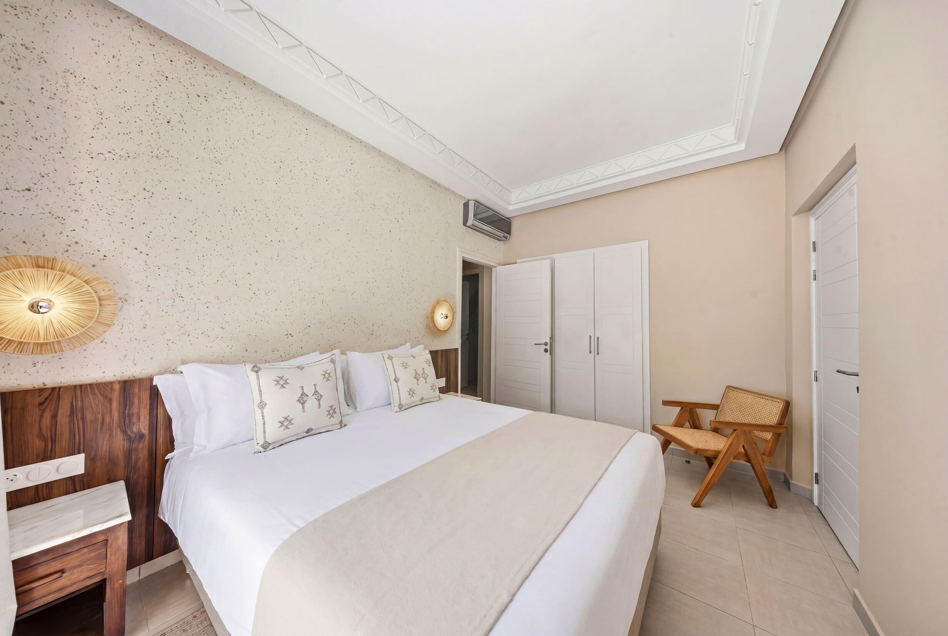A bedroom with a large bed, a wooden nightstand, a chair, and a wardrobe.
