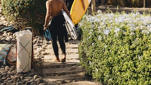 Un sendero que lleva a una playa con gente llevando tablas de surf.