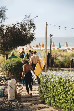 A pathway leading to a beach with people carrying surfboards.