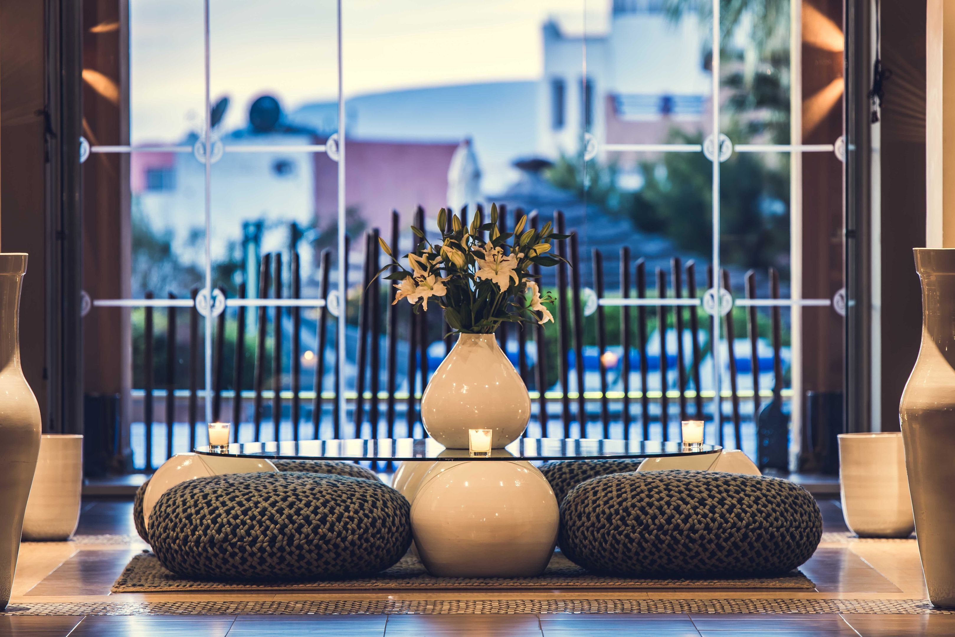A reception area with a large vase of flowers, a small table with a candle, and several textured cushions.