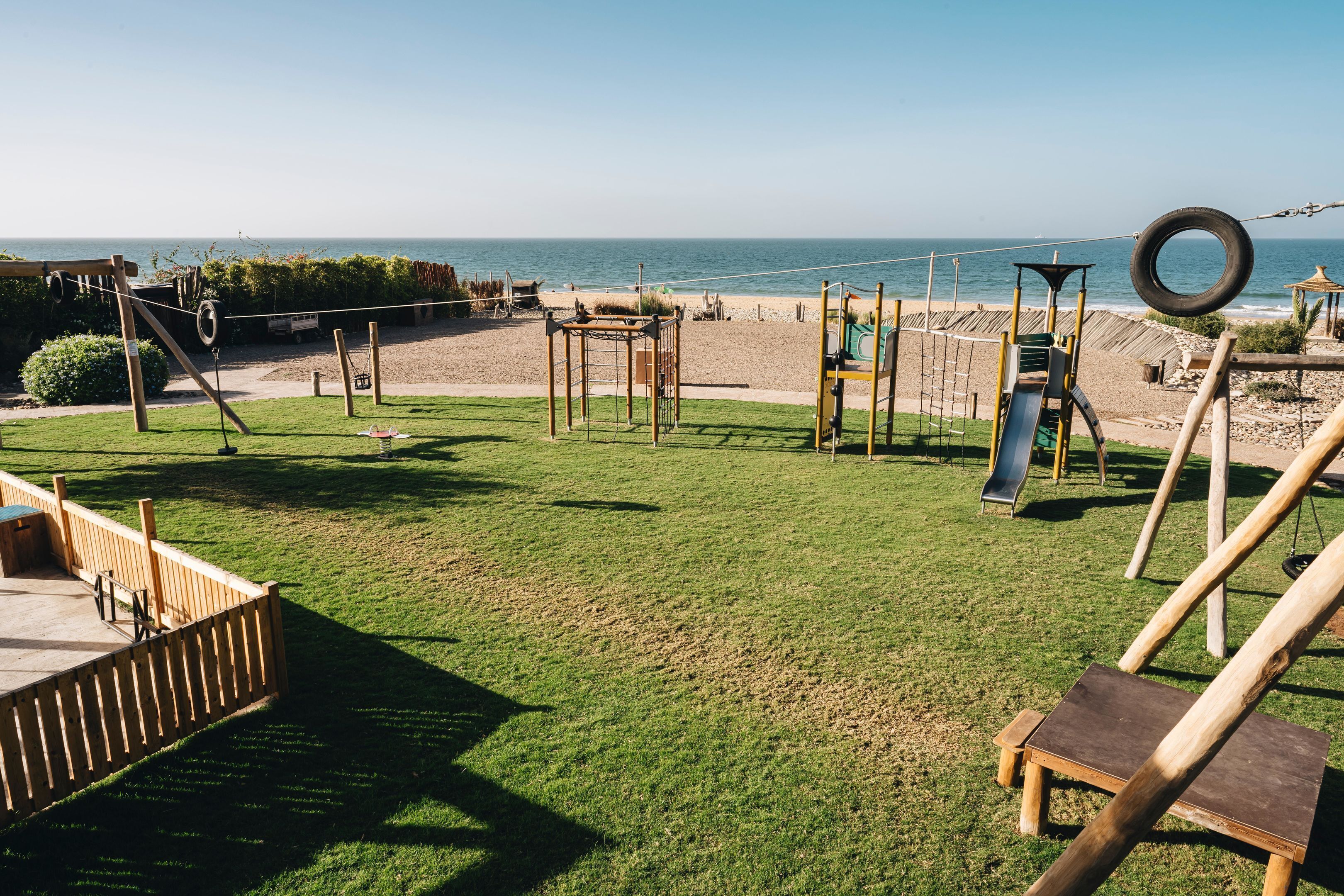 A playground with swings, slides, and climbing structures, overlooking a beach.