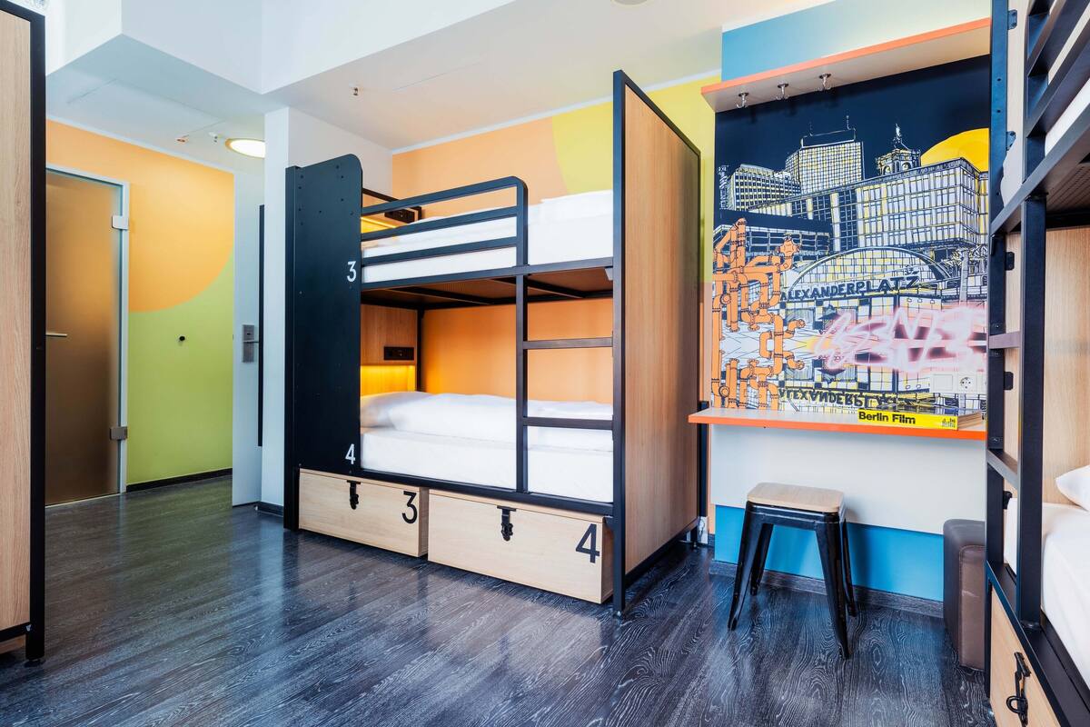 A bunk room with a cityscape mural, wooden bunk beds, and a small stool.