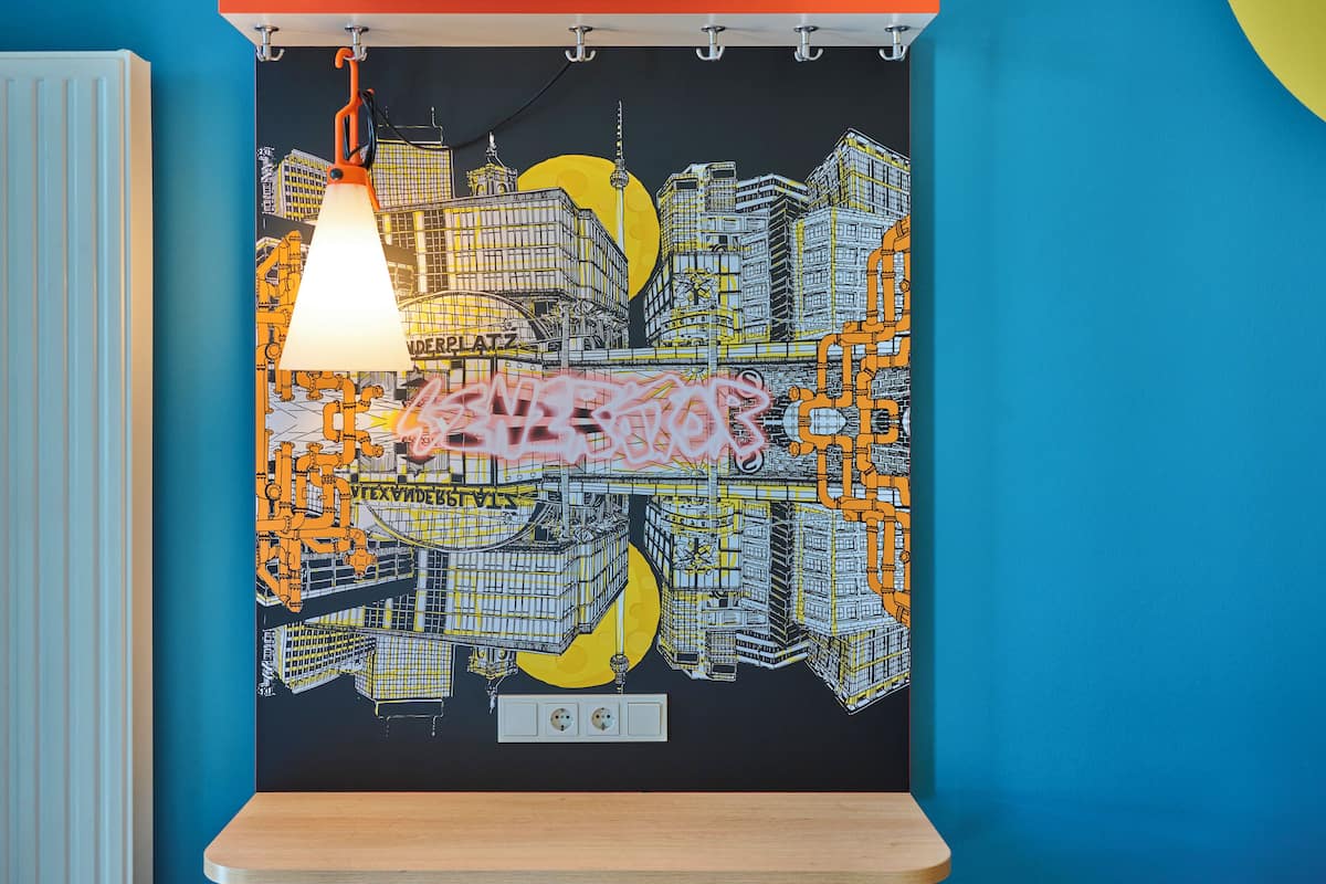 A wall with a cityscape mural, a hanging pendant light, and a wooden shelf.
