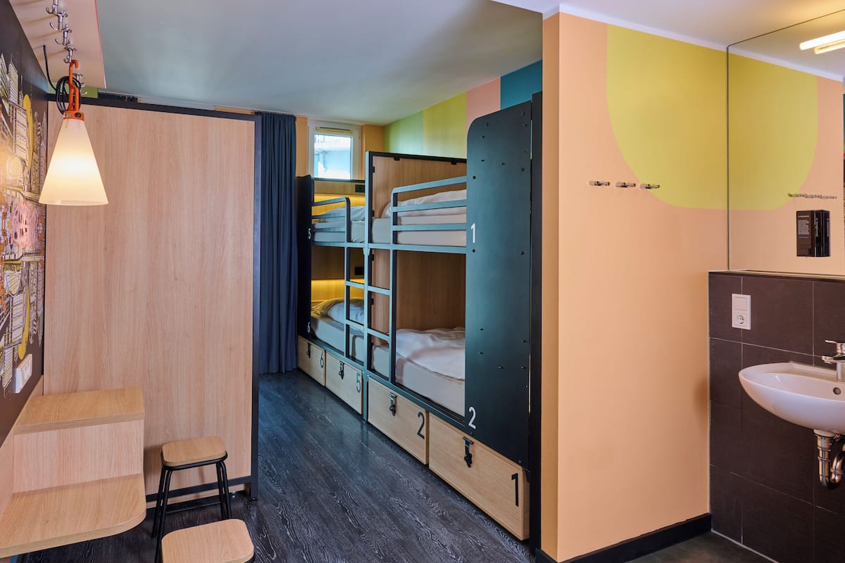 Habitació d'hotel amb llits superposats, escriptori, cadira, rentapel i mirall.